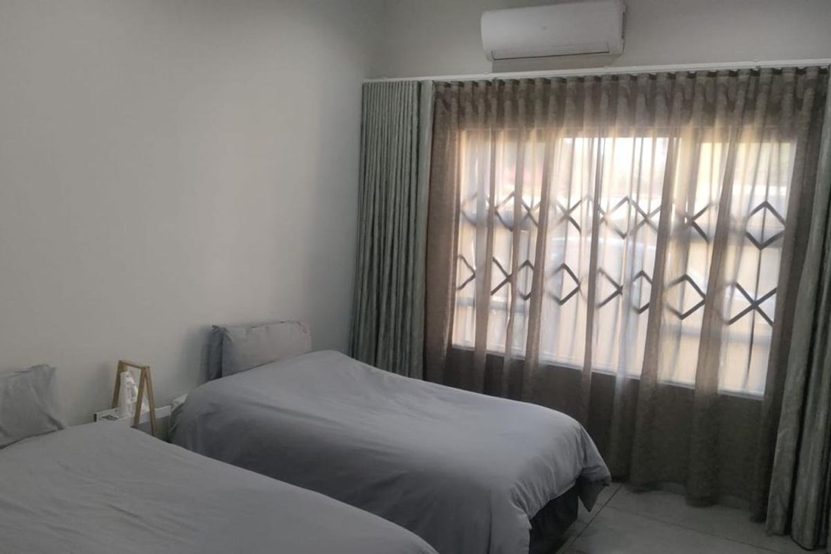 A well-maintained bedroom featuring floor-to-ceiling curtains, a wall-mounted air conditioning unit, and secure window burglar bars.