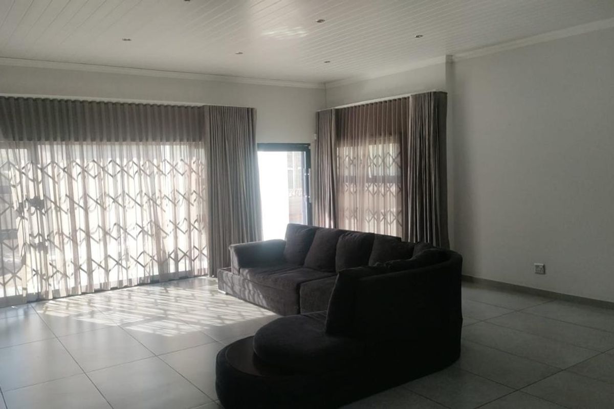 Spacious living room featuring large sliding glass doors with security gates, tiled flooring, and recessed ceiling lighting.