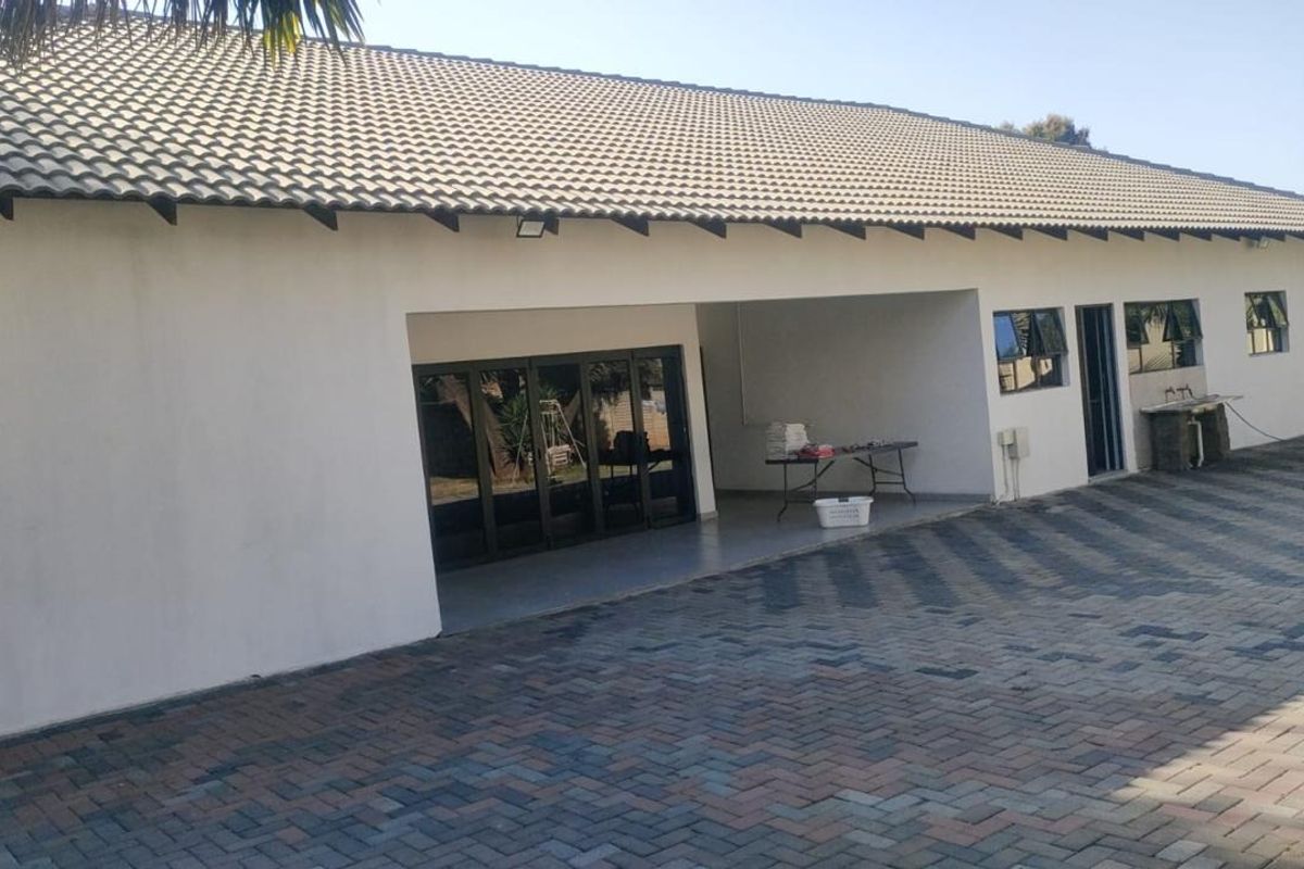 A view of the rear exterior featuring a paved driveway, a covered patio area with folding glass doors, and a tiled roof.