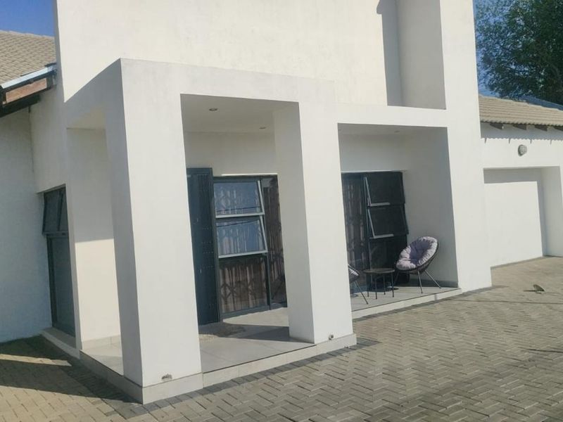 A modern front facade featuring a covered entrance, paved driveway, and clean white exterior finishes with aluminum window frames.