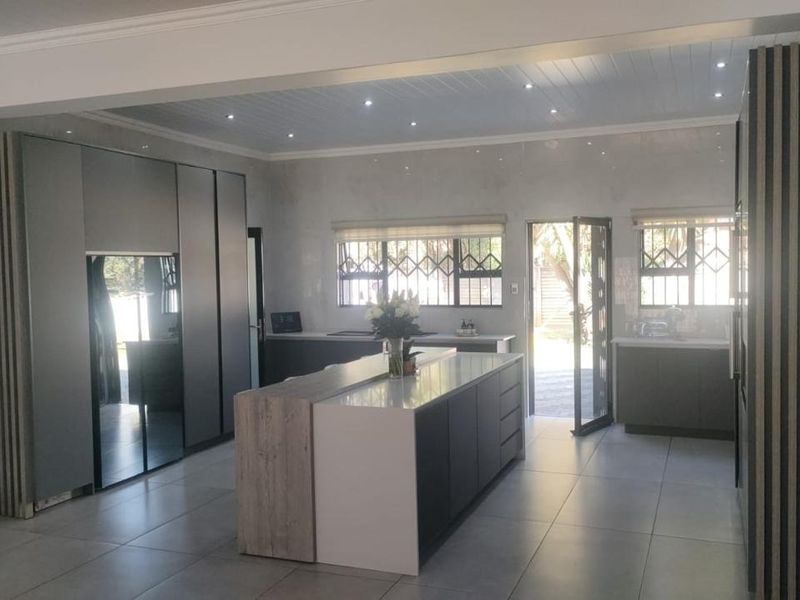 Modern kitchen featuring a central island, sleek built-in cabinetry, recessed lighting, and large format floor tiles with direct access to the exterior.