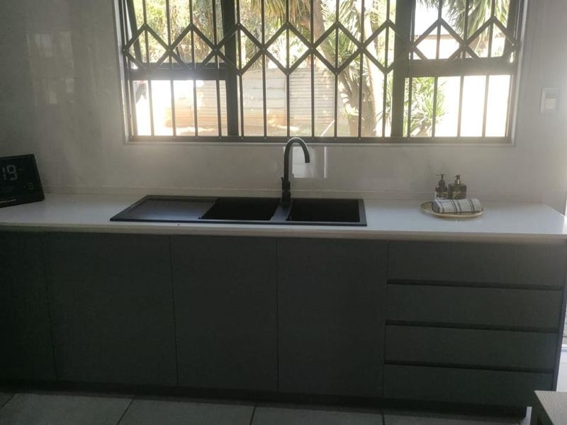 Modern kitchen area featuring sleek grey cabinetry, a white quartz countertop, and a contemporary black undermount double sink with a matching mixer tap.