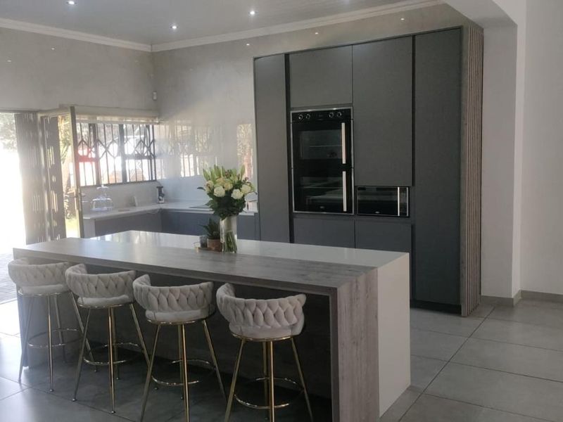 Modern kitchen featuring a large island with breakfast bar seating, sleek dark cabinetry, built-in appliances, and contemporary tiled flooring.