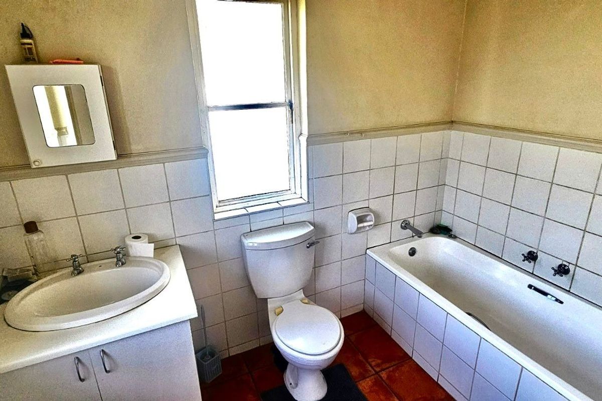 A dated bathroom featuring a built-in vanity with basin, a standard toilet, and a bathtub with wall-mounted shower mixer.