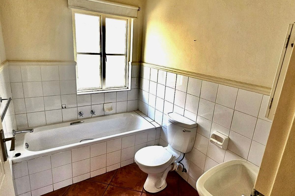 A dated bathroom featuring a built-in bathtub, standard toilet, and tiled walls, requiring cosmetic updates to modernize the space.