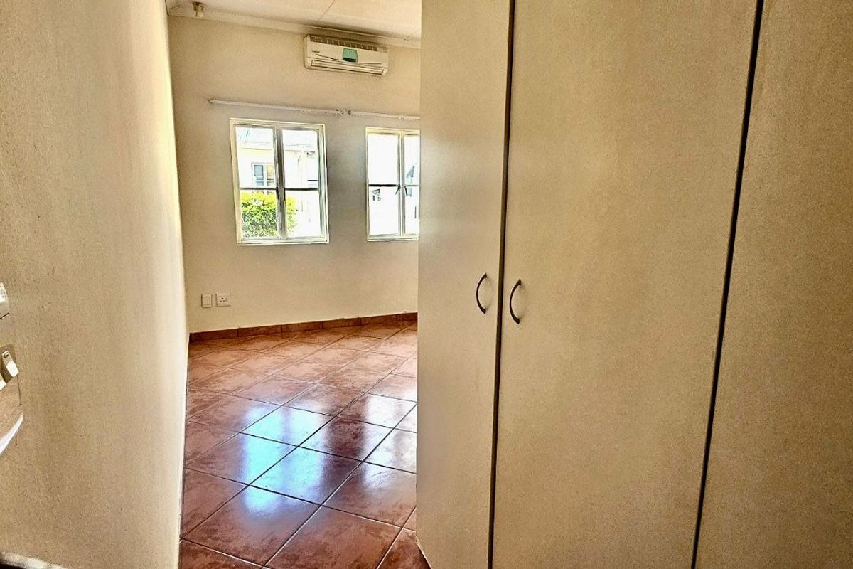 A bedroom featuring built-in cupboards, tiled flooring, and a wall-mounted air conditioning unit.
