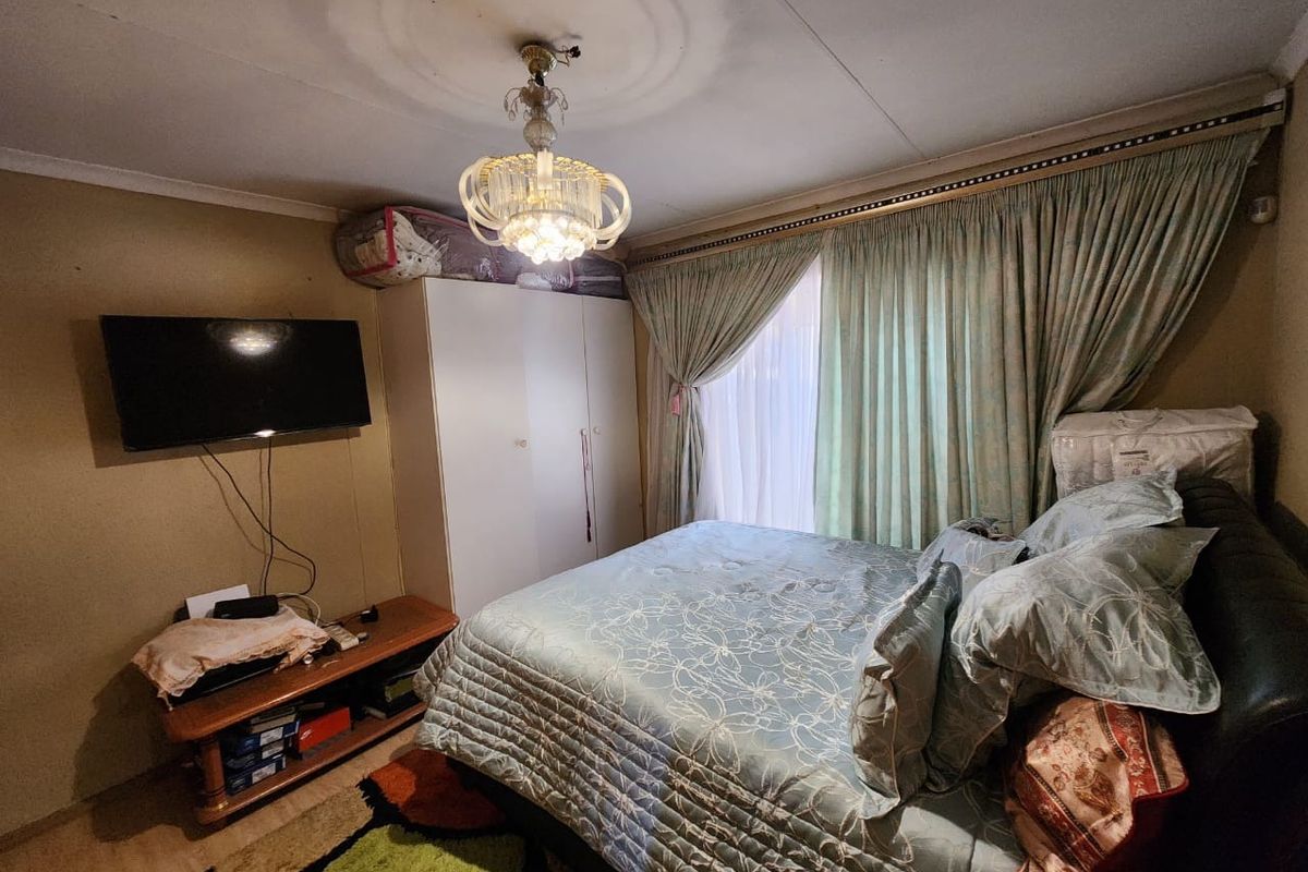 A bedroom featuring a built-in wardrobe, ceiling rose with chandelier, and window with curtain tracks.