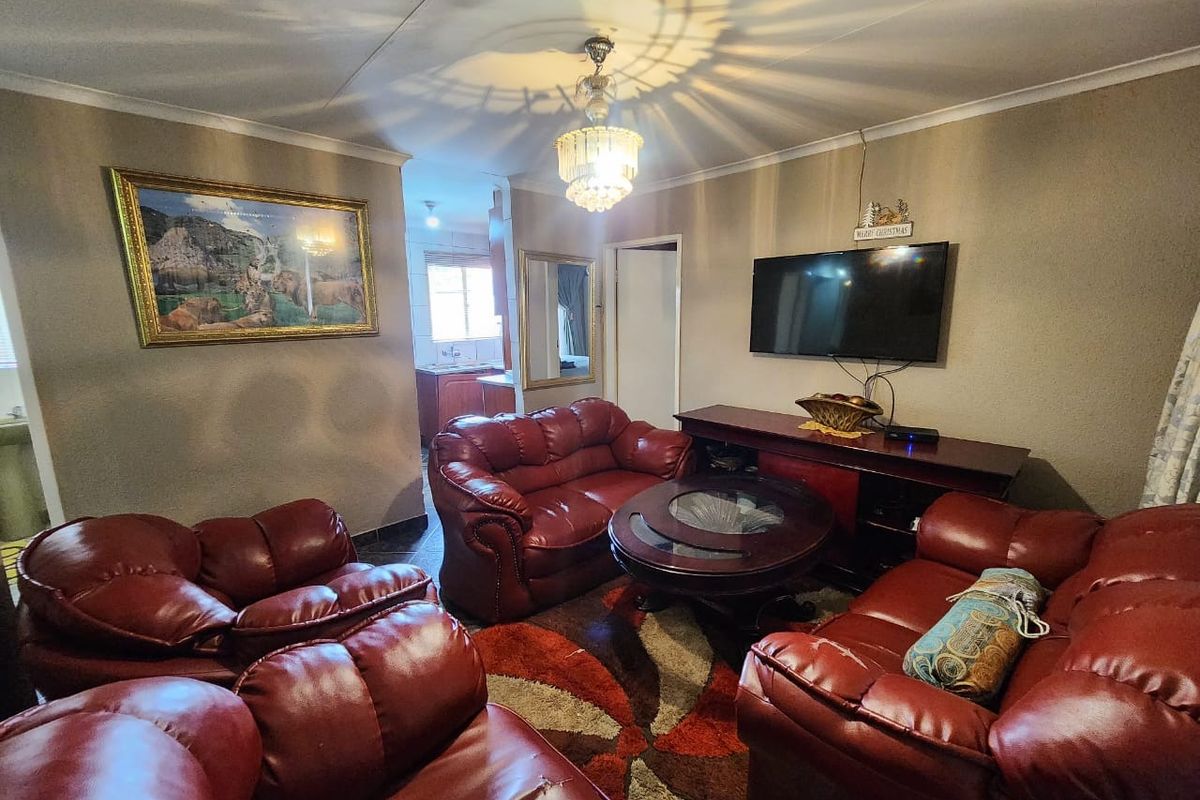 A comfortable living room featuring a central chandelier, crown molding, and a view through to the kitchen area.