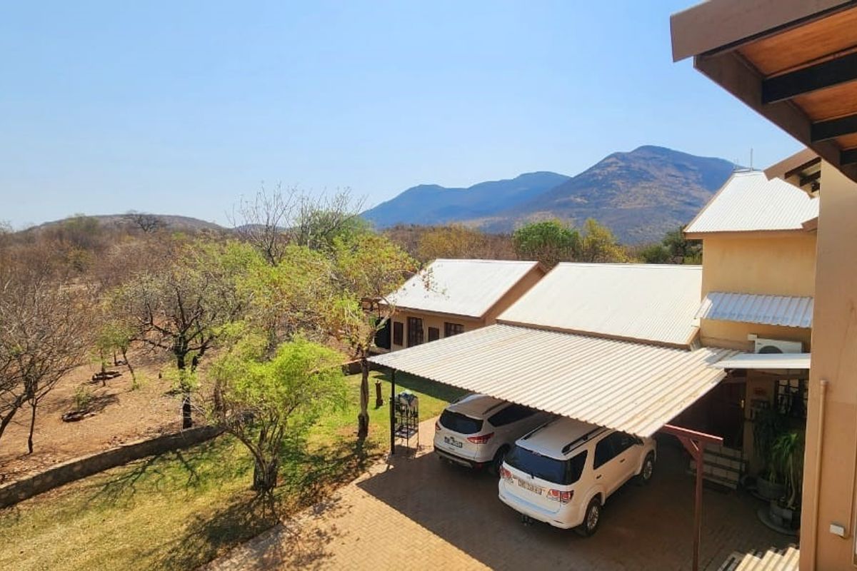 Elevated view of the farm property featuring a covered carport, metal roofing, and expansive natural landscape with mountain views.