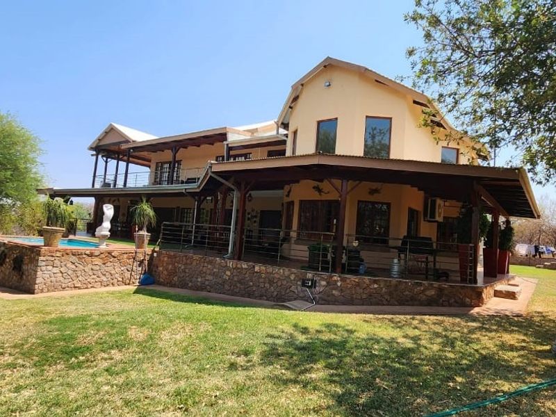 A spacious rear exterior view of the farm property featuring a large covered patio, stone-clad pool base, and expansive landscaped garden area.
