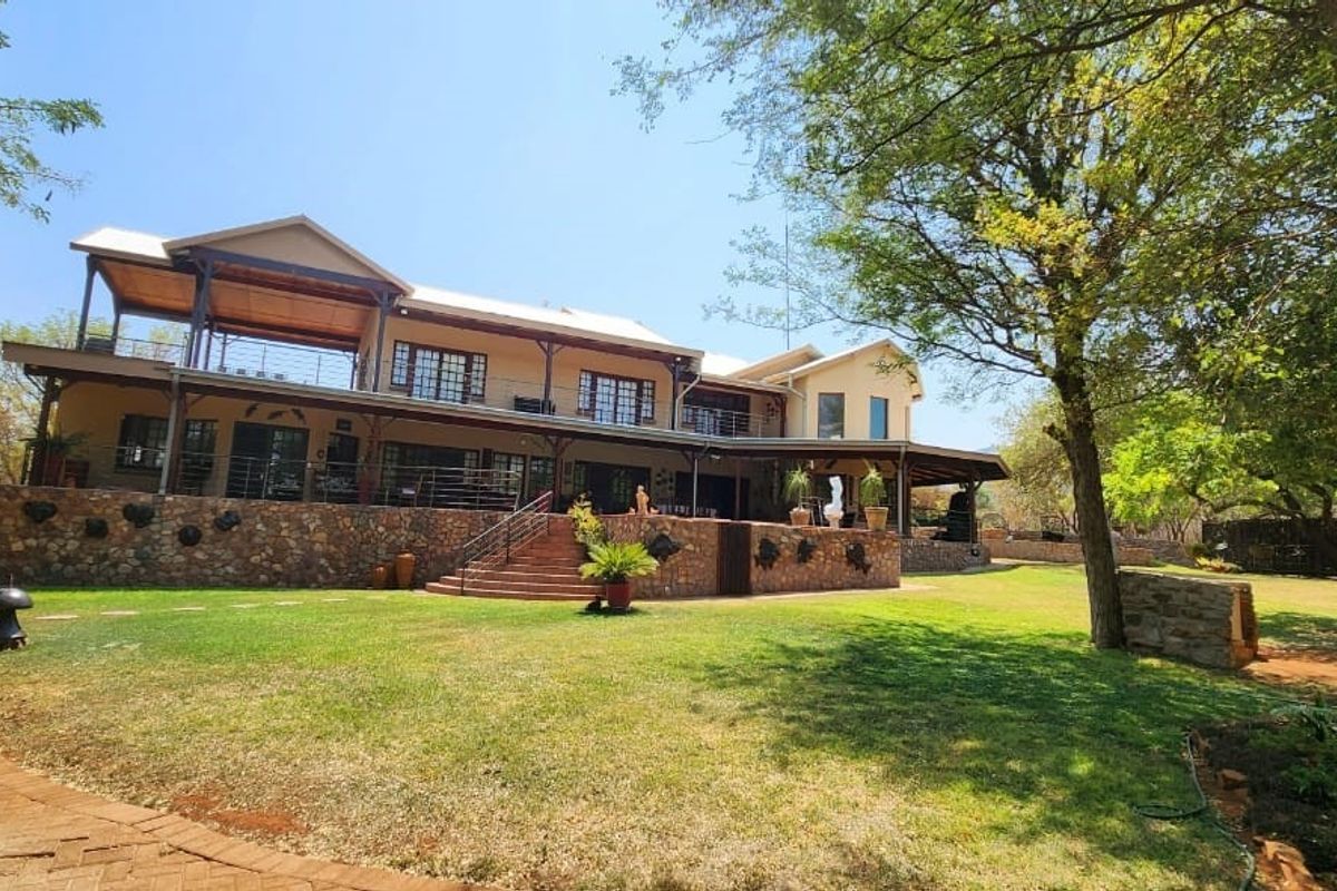 A spacious two-story farmhouse featuring stone cladding, expansive covered balconies, and a well-maintained garden setting.