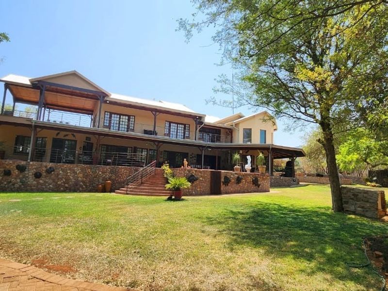A spacious two-story farmhouse featuring stone cladding, expansive covered balconies, and a well-maintained garden setting.