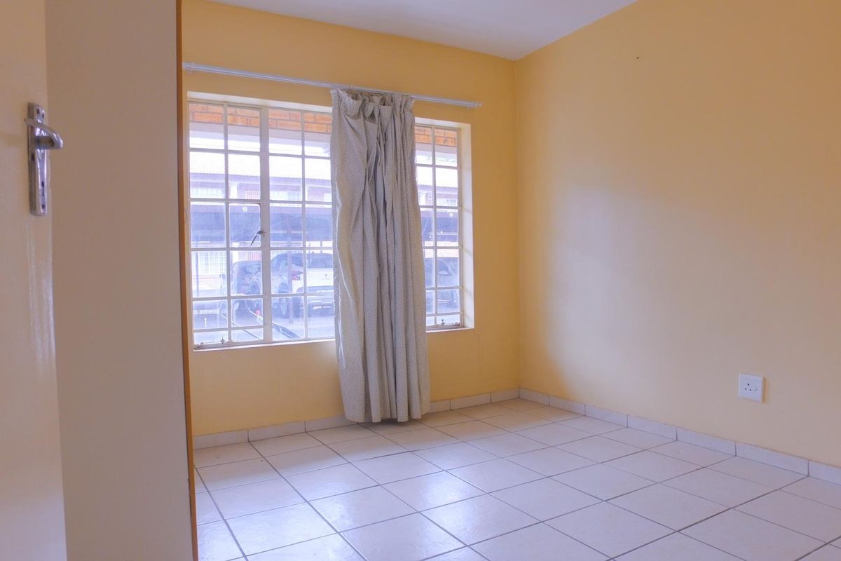 A vacant bedroom featuring tiled flooring, yellow painted walls, and a large window with security bars, offering a blank canvas for personalization.