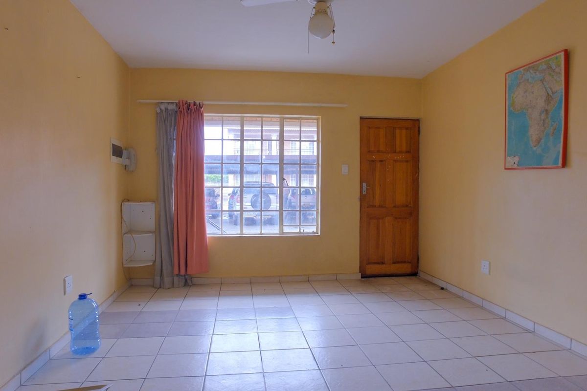 A vacant living room featuring tiled flooring, a large window with security bars, and a wooden entrance door.