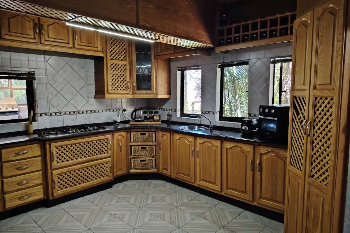 A traditional kitchen featuring solid wood cabinetry, dark granite countertops, integrated gas hob, and tiled flooring with a classic layout.