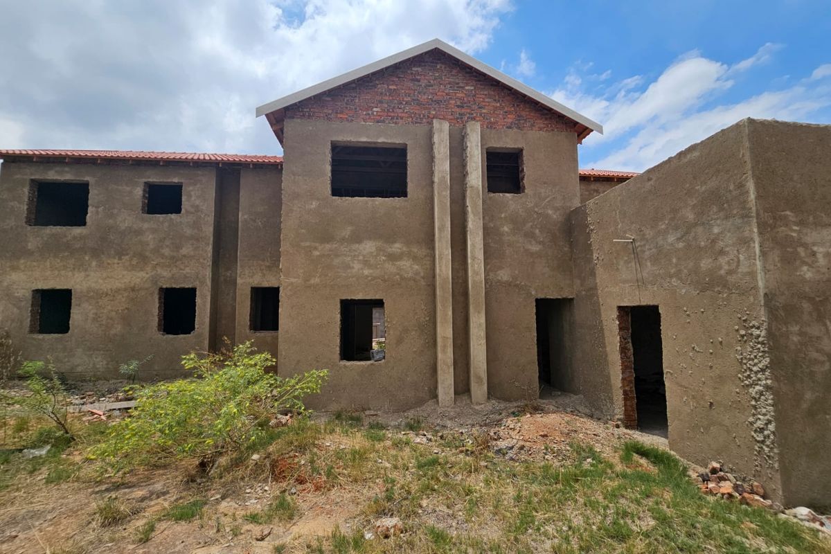 A double-story residential property currently under construction, featuring raw plaster finishes, exposed brickwork, and open window and door apertures.