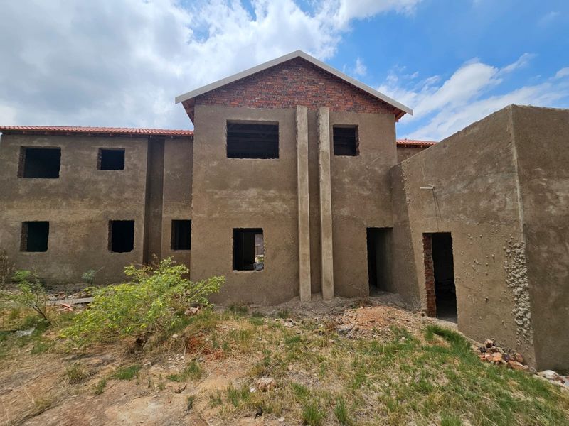 A double-story residential property currently under construction, featuring raw plaster finishes, exposed brickwork, and open window and door apertures.