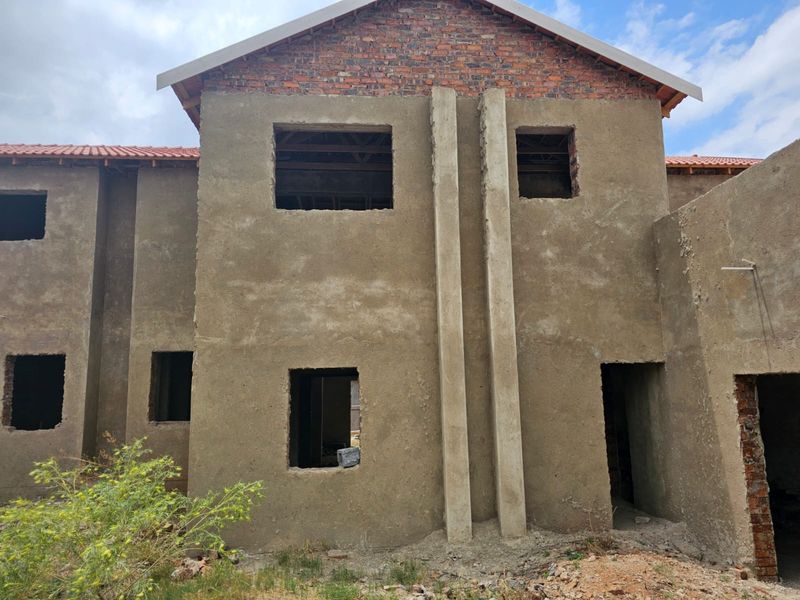 Exterior view of a residential property under construction, featuring raw plastered walls, exposed brickwork, and open window and door apertures.