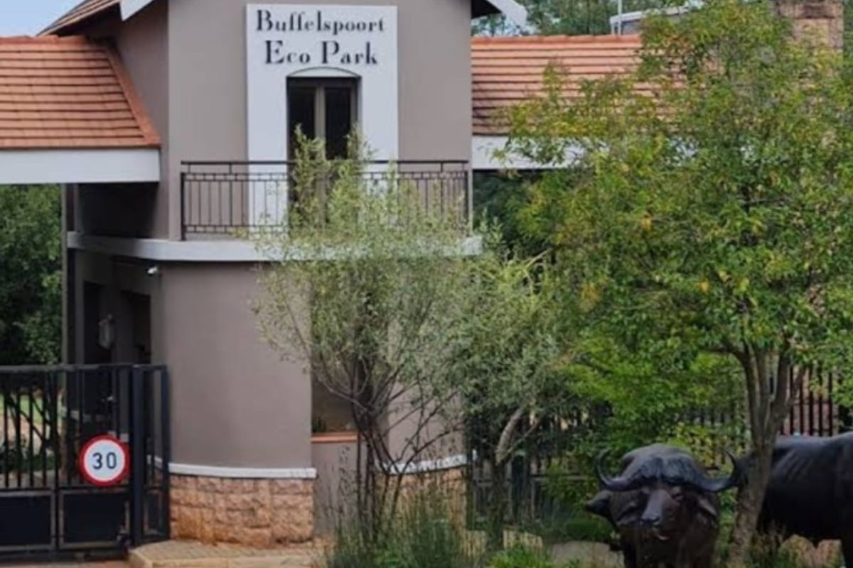 The entrance gatehouse of Buffelspoort Eco Park, featuring a paved driveway, security access control, and landscaped surroundings.