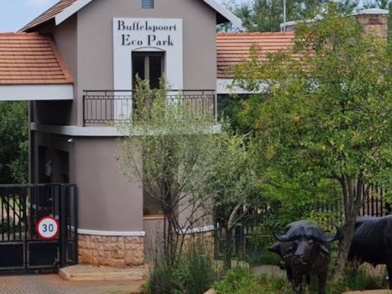 The entrance gatehouse of Buffelspoort Eco Park, featuring a paved driveway, security access control, and landscaped surroundings.