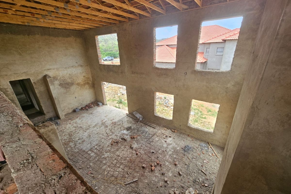 An unfinished double-volume interior space under construction, featuring exposed roof trusses, raw plaster walls, and open window apertures.