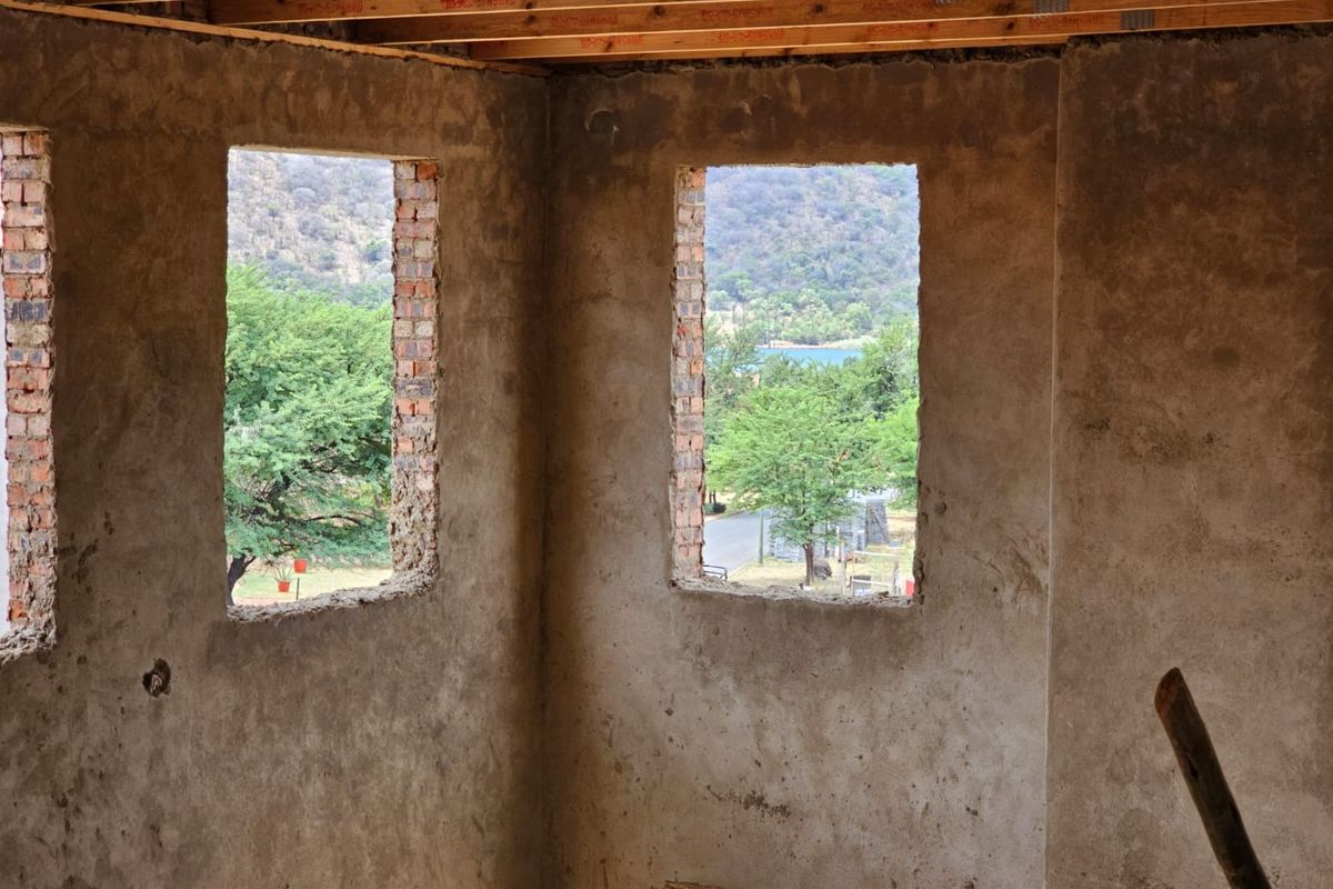 An interior view of a room under construction, featuring exposed concrete walls, open window apertures, and visible timber ceiling joists.