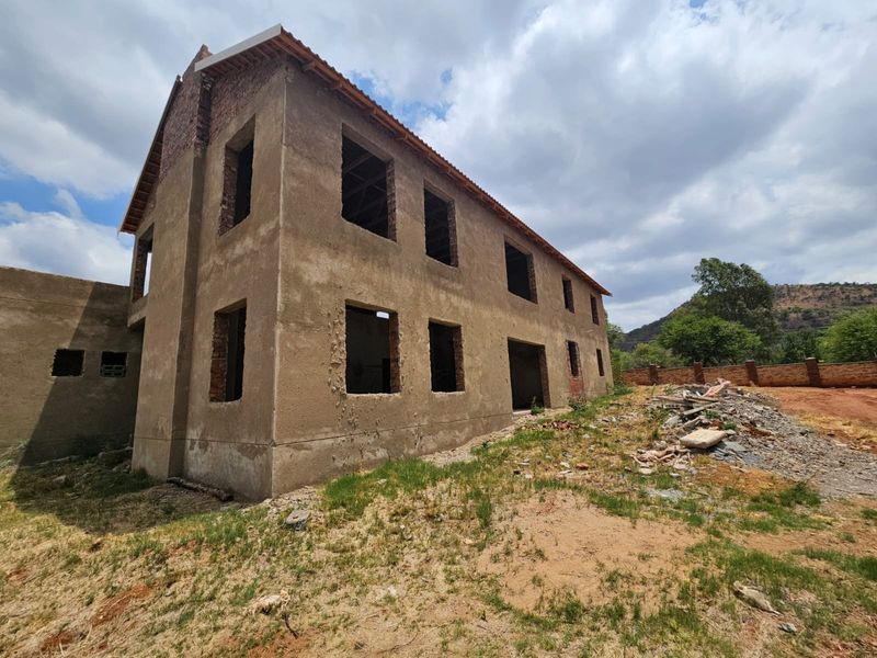 A two-story residential property under construction, featuring an unfinished exterior shell, exposed brickwork, and open window and door apertures.