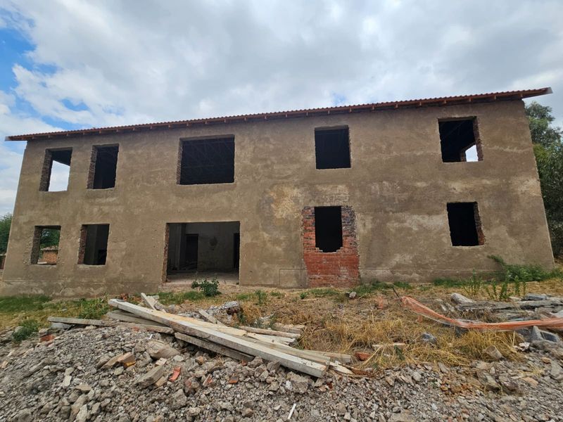 A two-story residential property under construction, featuring an unfinished exterior facade, exposed brickwork, and open window and door apertures.