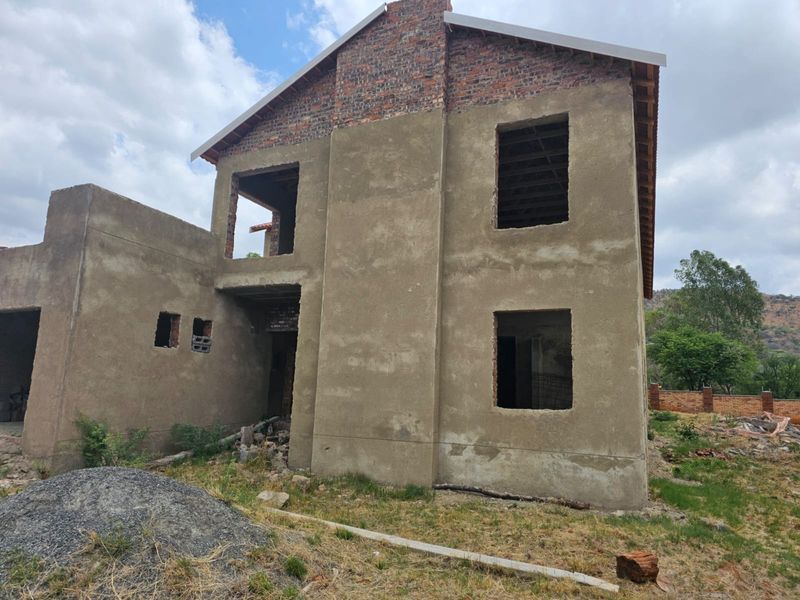 A two-story residential property under construction, featuring exposed brickwork, unfinished plaster, and open window and door apertures.