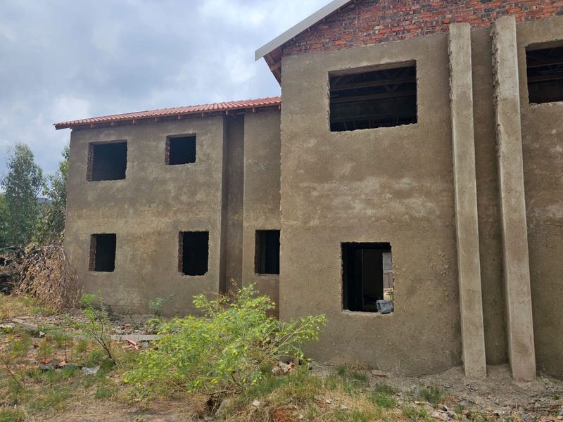 A two-story residential property under construction, featuring raw plastered walls, exposed brickwork, and open window apertures awaiting installation.