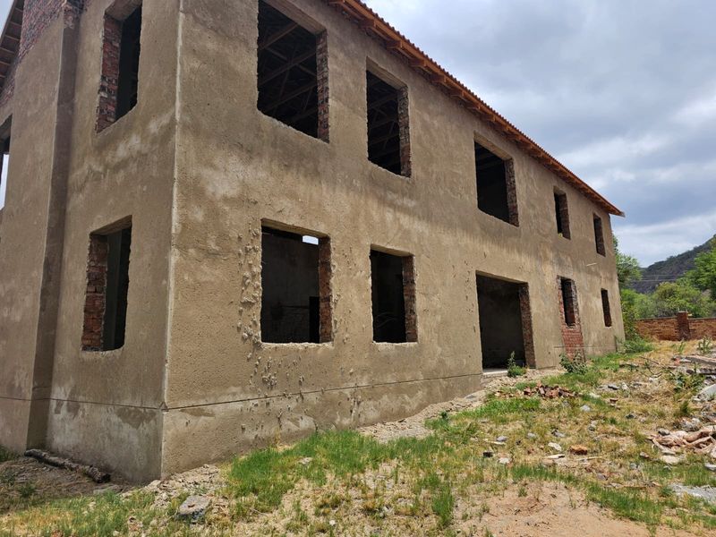 A two-story residential structure in the early stages of construction, featuring raw plaster walls and open window frames awaiting final finishes.