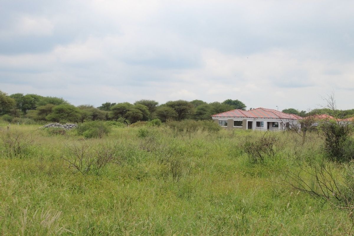 A view of a residential property set within a large, undeveloped grassy plot with surrounding trees and natural vegetation.