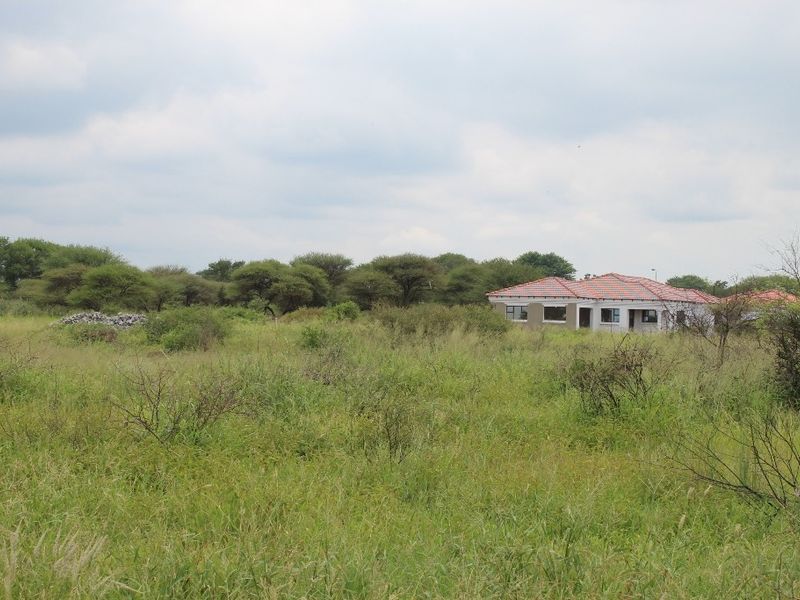 A view of a residential property set within a large, undeveloped grassy plot with surrounding trees and natural vegetation.