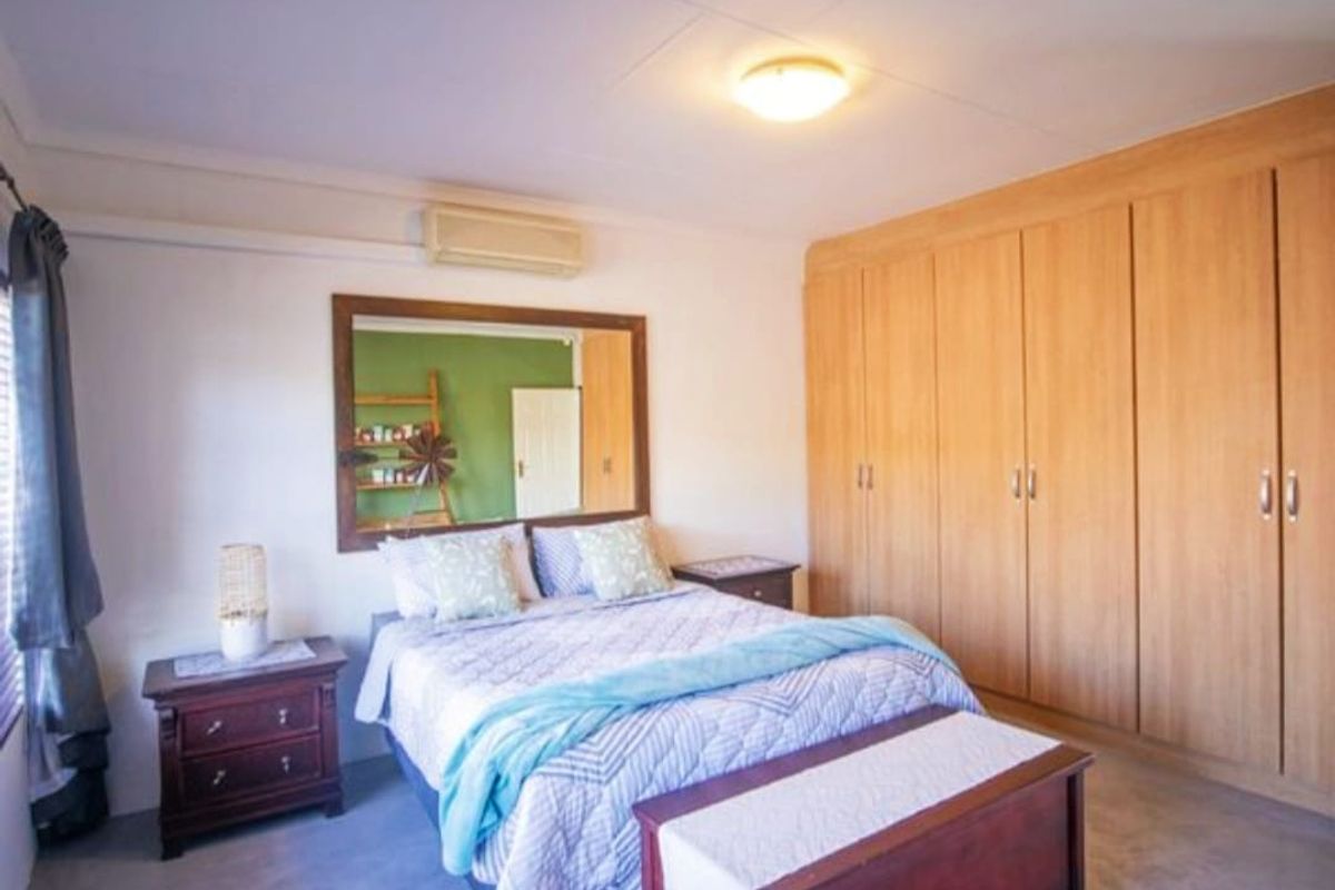 A bedroom featuring built-in wooden cupboards, a wall-mounted air conditioning unit, and a large mirror, providing functional storage and climate control.