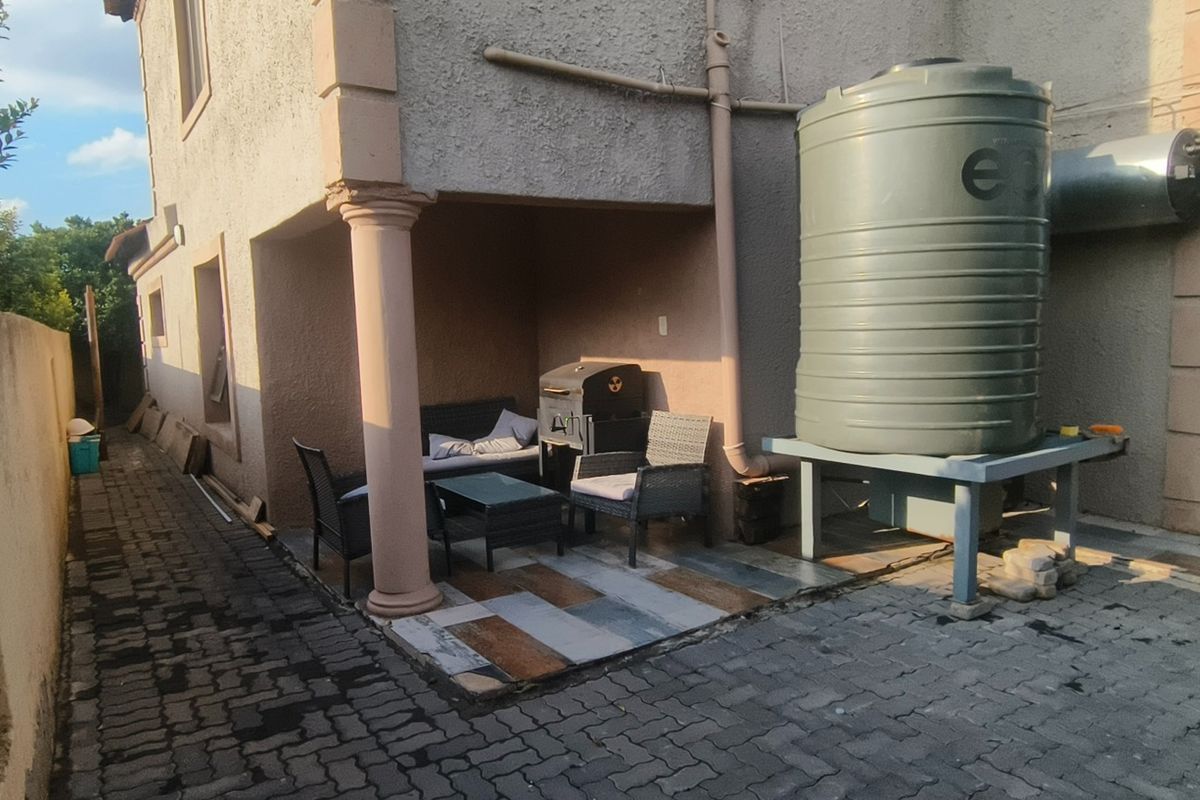 A rear patio area featuring a covered seating space, paved flooring, and an external water storage tank with a supporting stand.