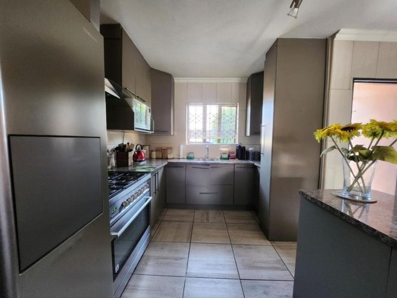 A functional kitchen featuring modern grey cabinetry, granite countertops, a gas stove with extractor fan, and tiled flooring.
