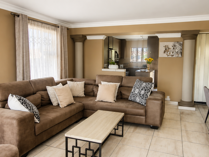Open-plan living and dining area featuring ceramic floor tiles, decorative columns, and an integrated kitchen, with a staircase leading to the upper level.