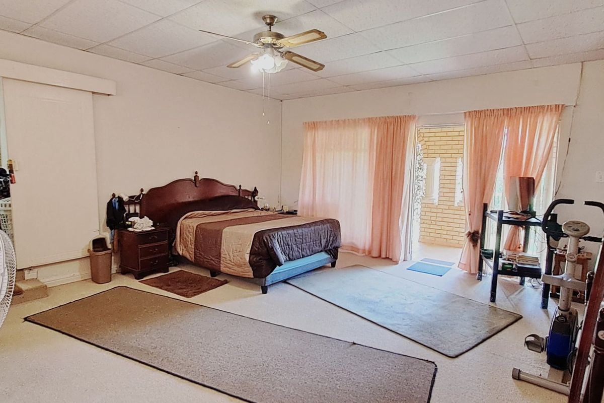 Spacious bedroom featuring a ceiling fan, exposed brick feature wall, and direct access to an outdoor patio area through sliding glass doors.
