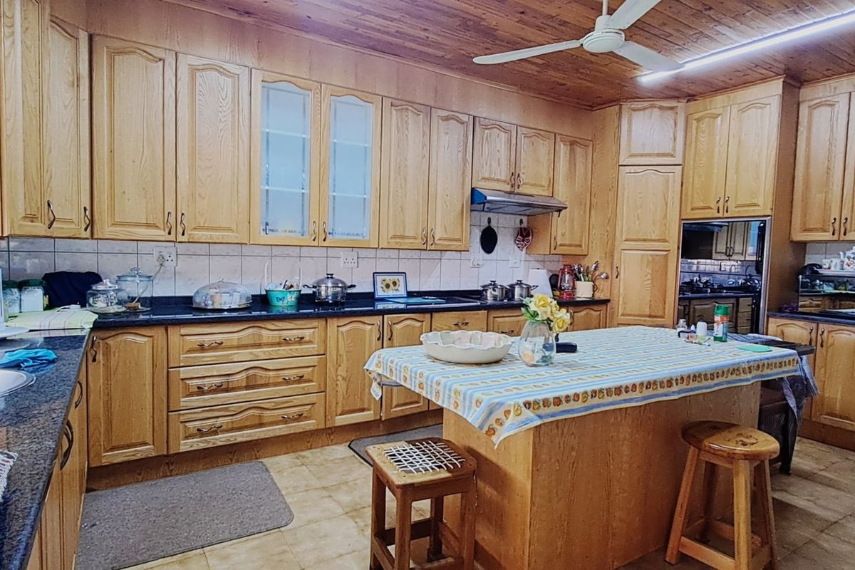 Spacious kitchen featuring extensive timber cabinetry, dark granite countertops, tiled flooring, and a central island with a built-in ceiling fan.