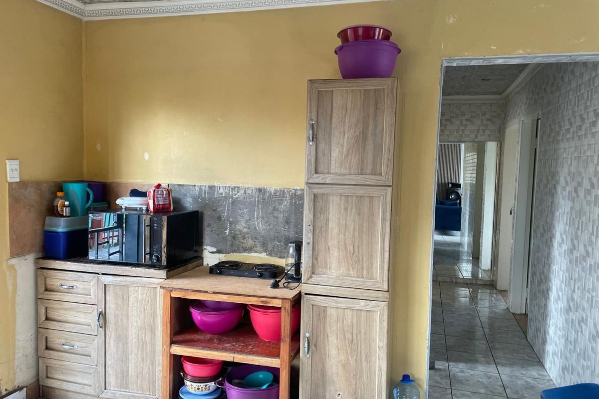 A compact kitchen area featuring wooden cabinetry, a portable cooktop, and a tiled hallway transition, requiring cosmetic updates to the walls and finishes.