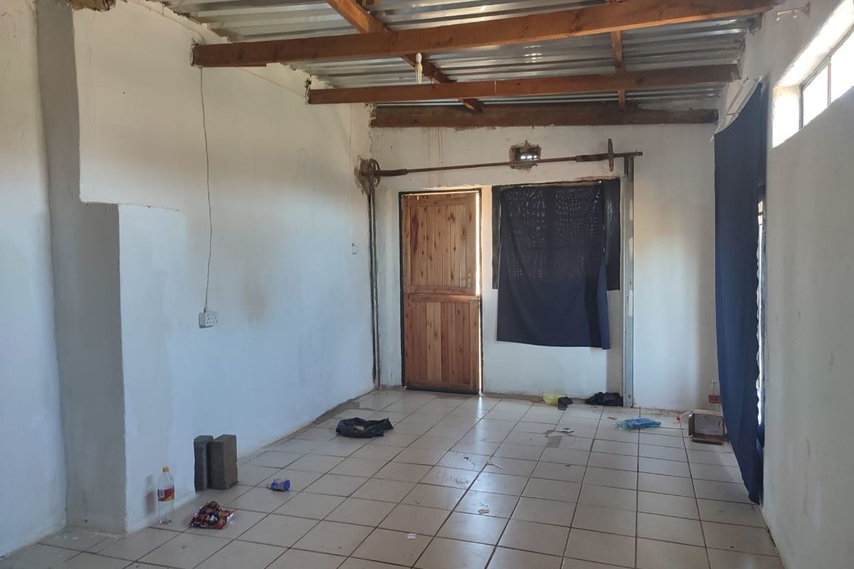An empty, unfinished living space featuring tiled flooring, exposed timber ceiling rafters, and a wooden entrance door.
