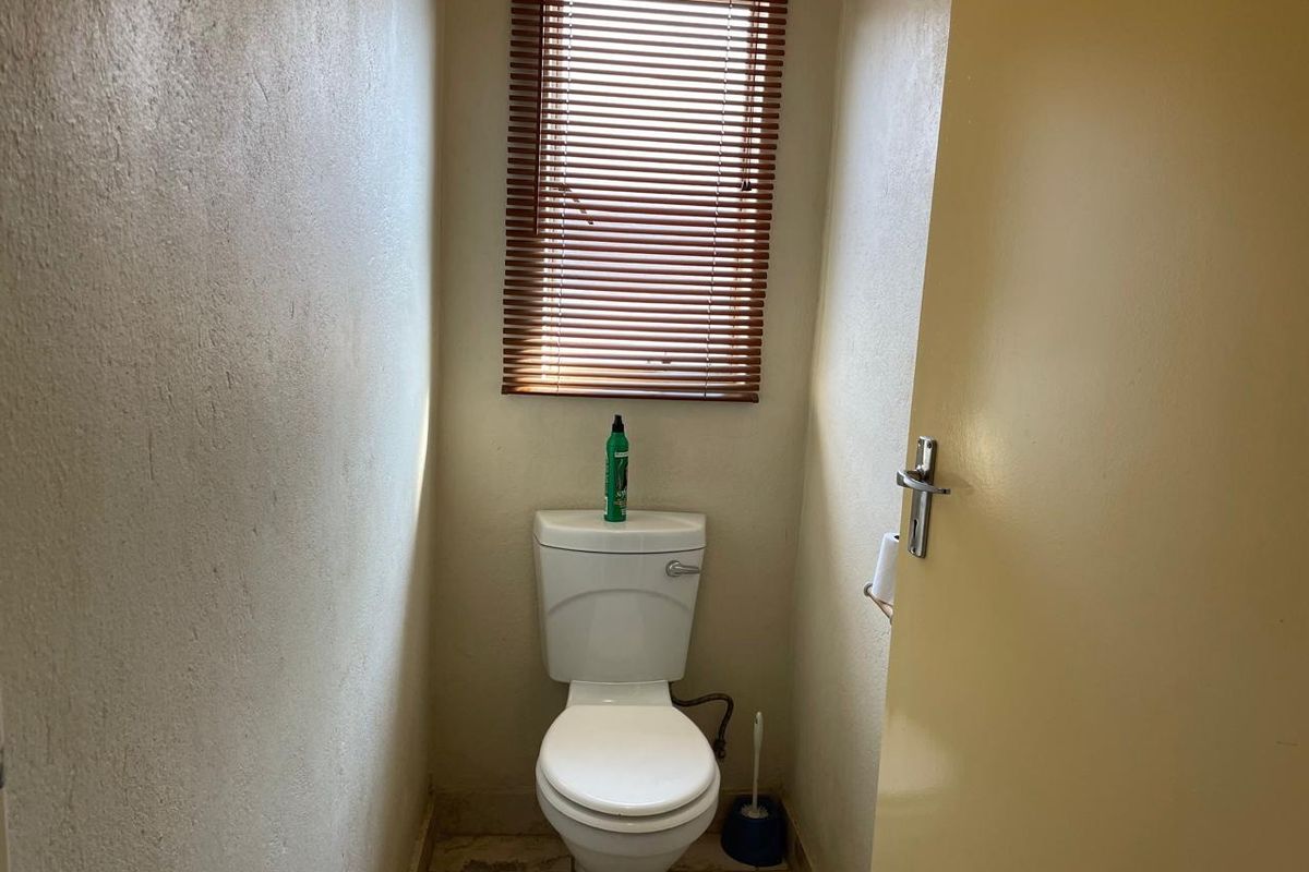 A compact, functional guest toilet featuring a standard white ceramic toilet suite and a window with fitted wooden blinds.