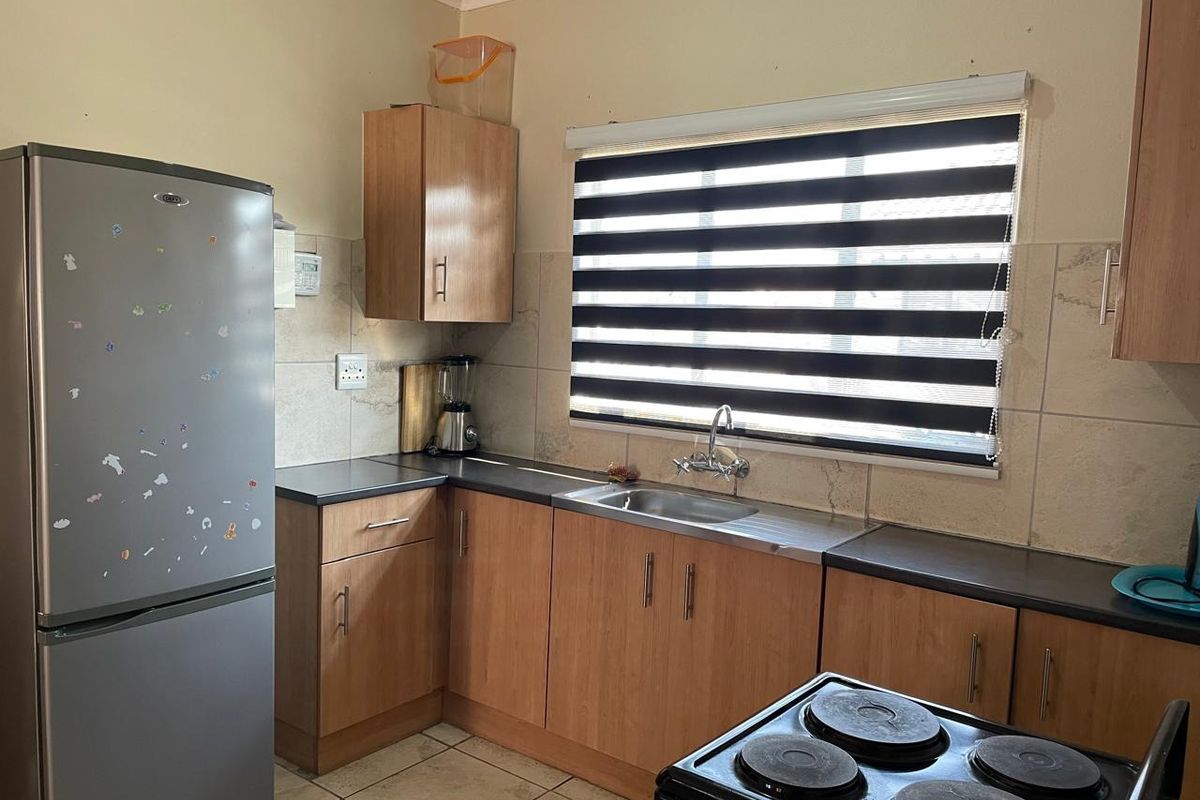A functional kitchen featuring wood-look cabinetry, dark laminate countertops, tiled splashbacks, and a stainless steel sink with a window view.