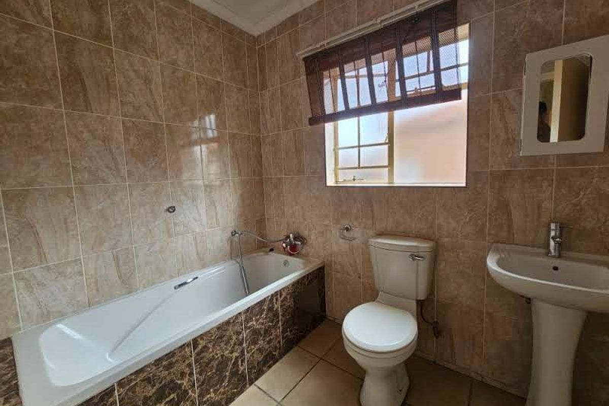 A functional bathroom featuring a built-in bathtub, pedestal basin, and toilet, finished with full-height wall tiling and a window for natural light.