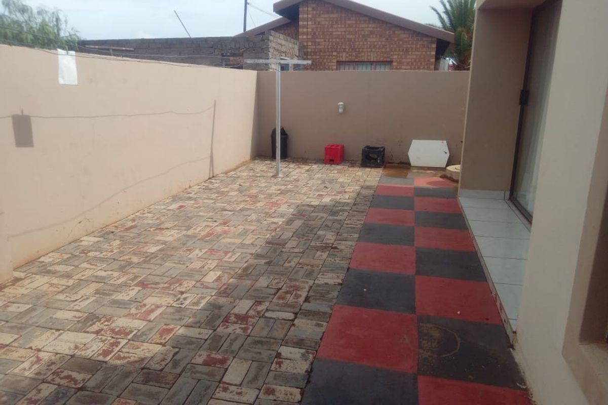 A paved rear courtyard area featuring a mix of brick and tiled surfaces, enclosed by a high boundary wall with sliding door access.