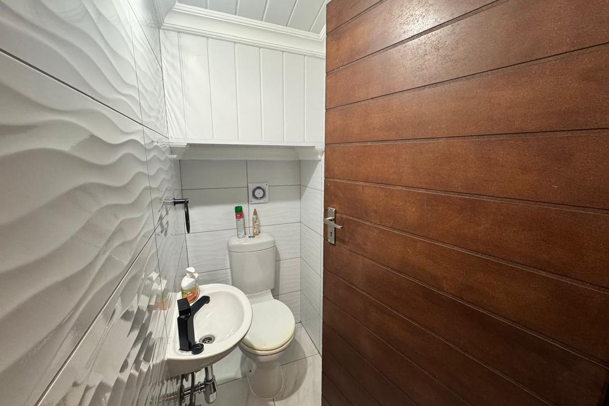 Compact guest bathroom featuring modern textured wall tiles, a wall-mounted basin with black tapware, and a wooden door.