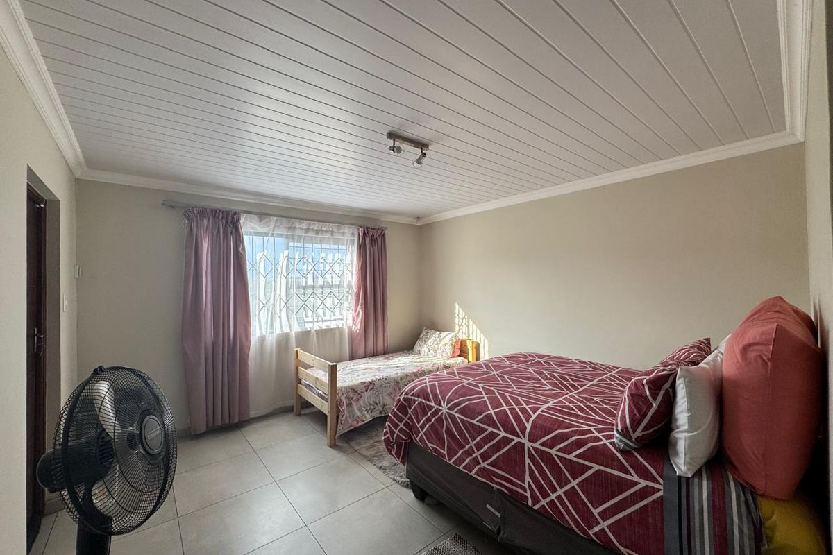 A spacious bedroom featuring tiled flooring, a white tongue-and-groove ceiling, and a window fitted with security bars.