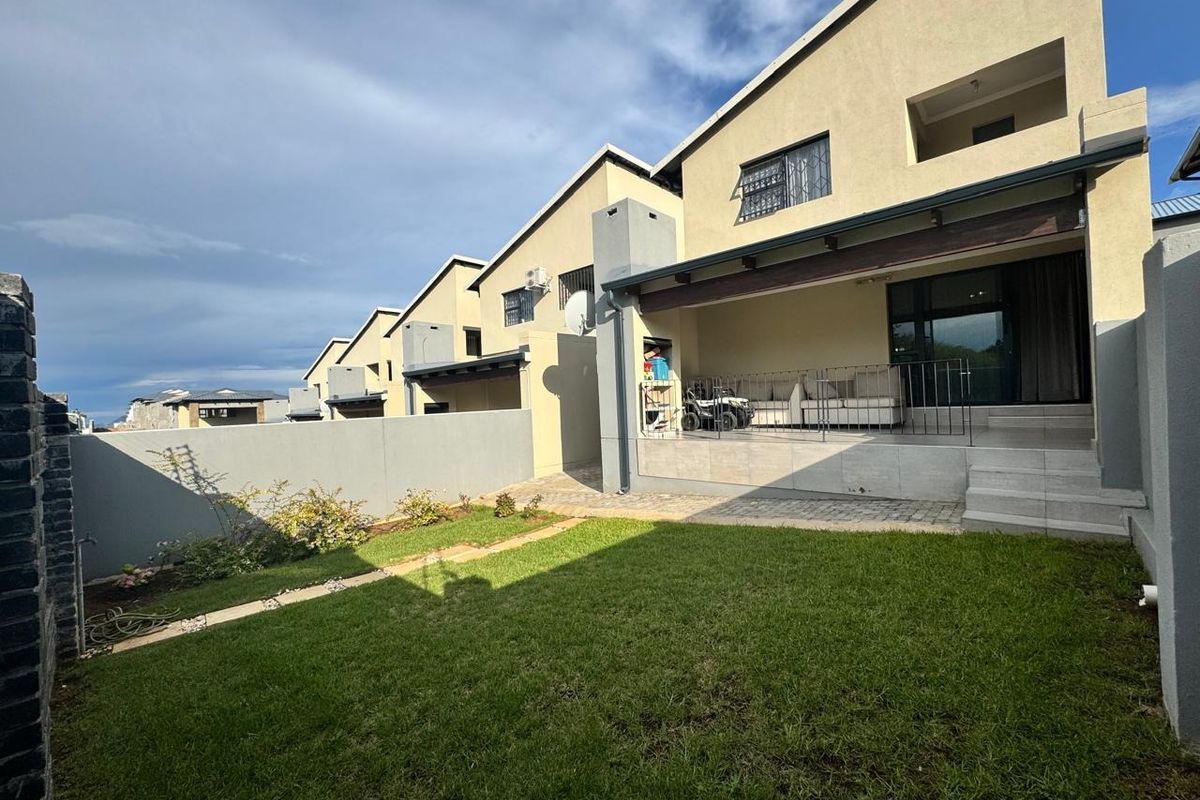 Rear view of the townhouse featuring a covered patio, paved area, and a private garden with perimeter walling.