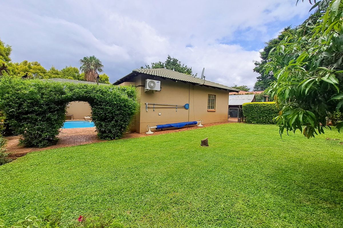 A well-maintained rear garden featuring a lush lawn, a swimming pool area, and an exterior wall with a mounted air conditioning unit.