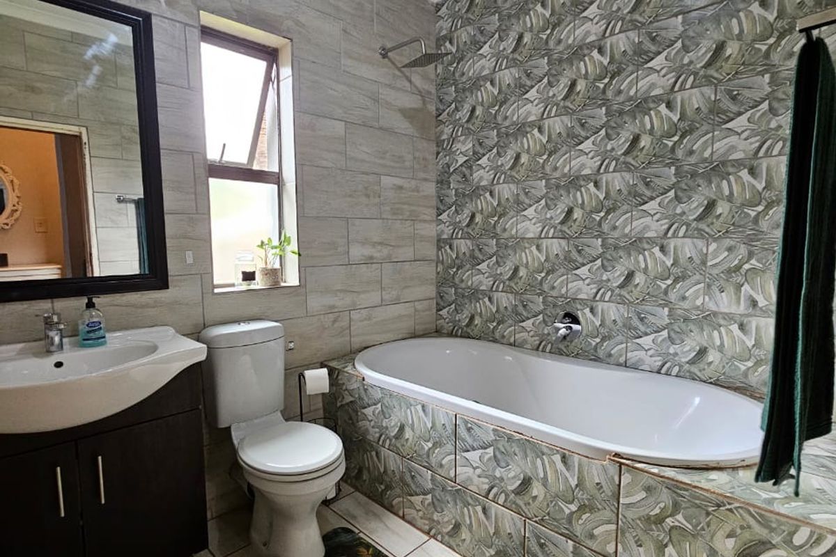 A bathroom featuring a built-in bathtub with decorative leaf-patterned tiling, a vanity basin, and a toilet, finished with neutral wall tiles.
